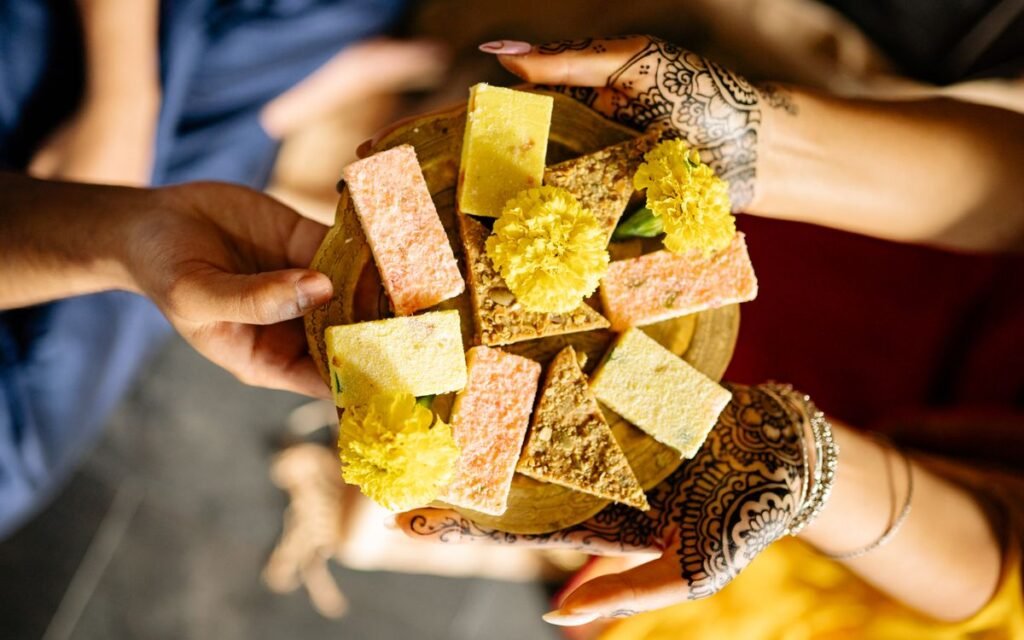 Hands holding a plate of Indian sweets and marigold flowers during Diwali