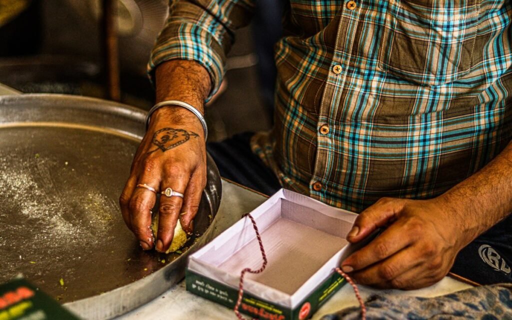 A sweet seller's hands shaping mithai next to an open gift box