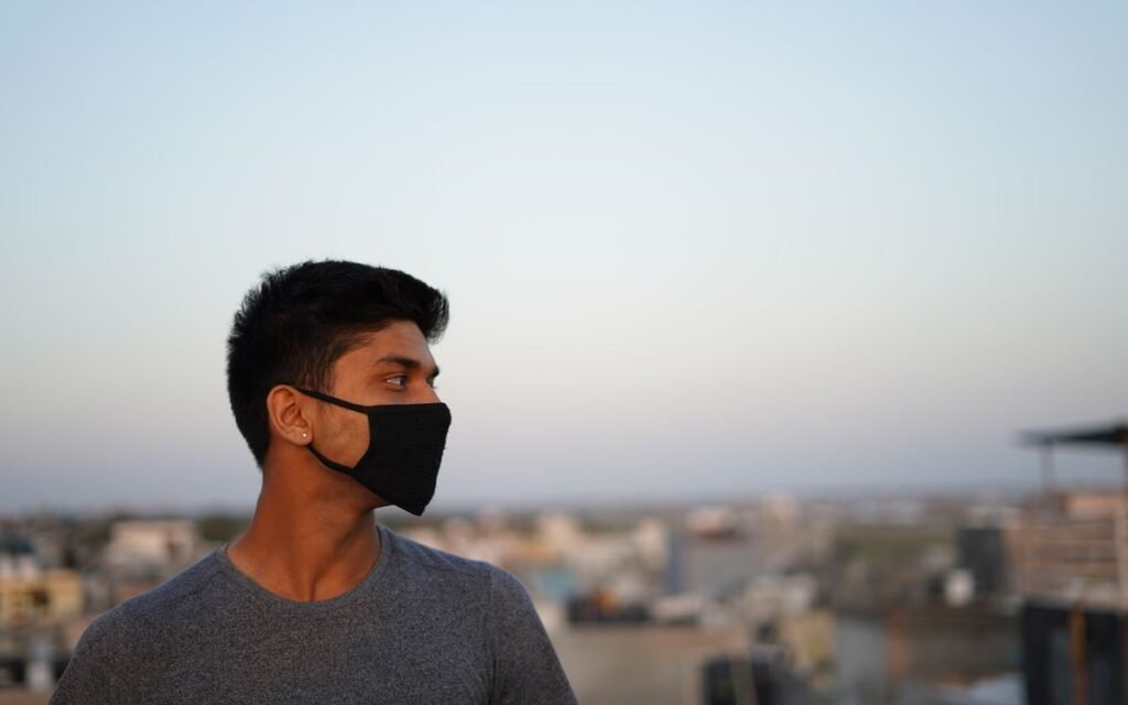 A young man wearing a black face mask on a rooftop with a hazy city behind him