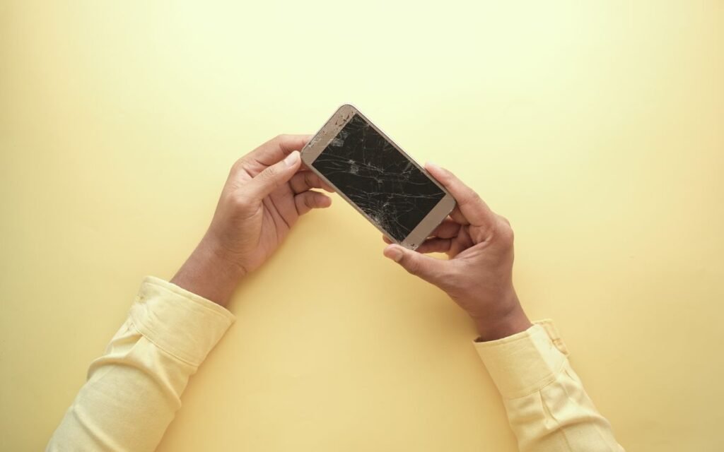 Hands holding a smartphone with a badly cracked screen