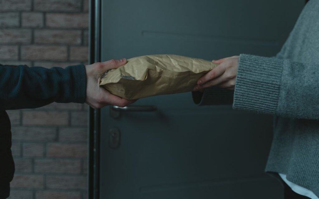 Hands passing a paper parcel at a front door