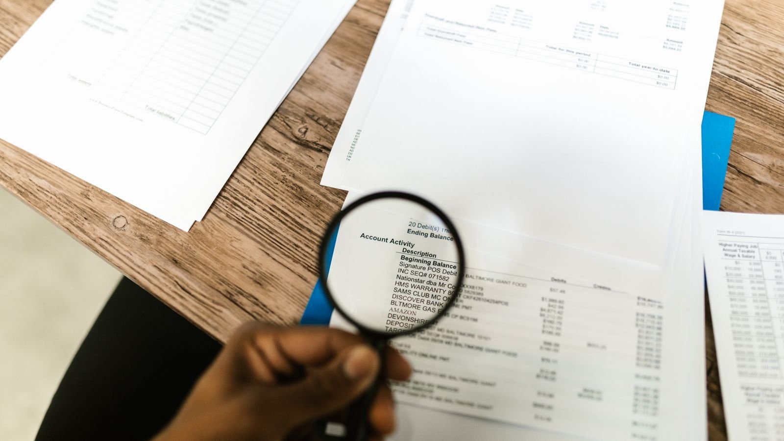 A hand holding a magnifying glass over a printed account statement