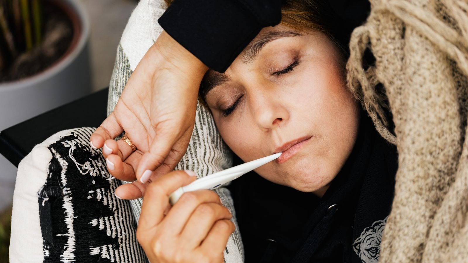 Woman with a fever checking her temperature with a thermometer