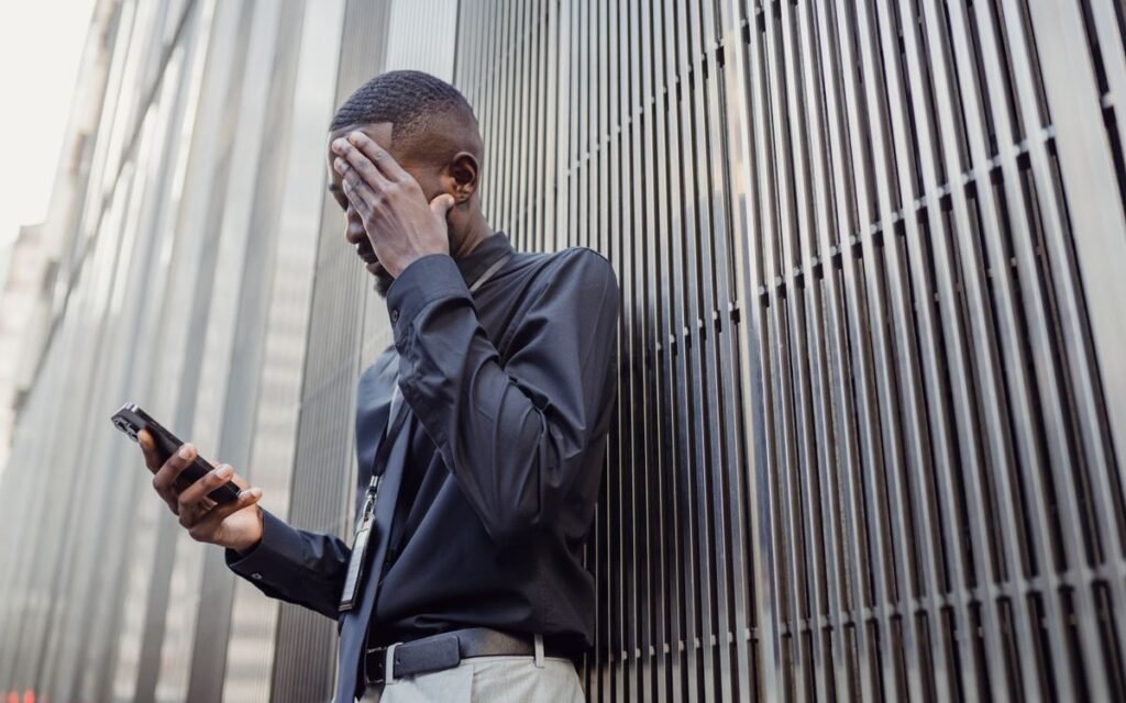 Man leaning on a wall, covering his face while holding a phone