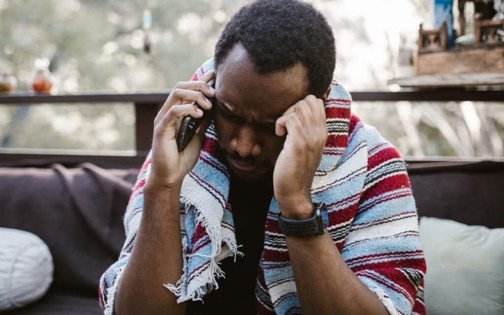 Stressed man wrapped in a striped blanket holding his head during a phone call