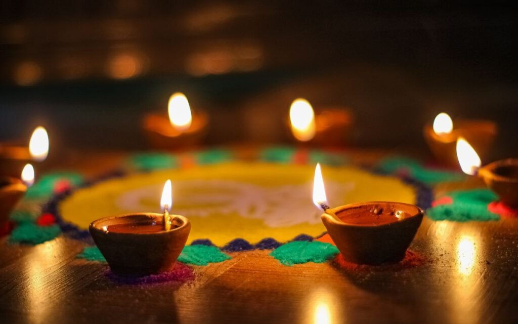 lit diyas around a colourful rangoli