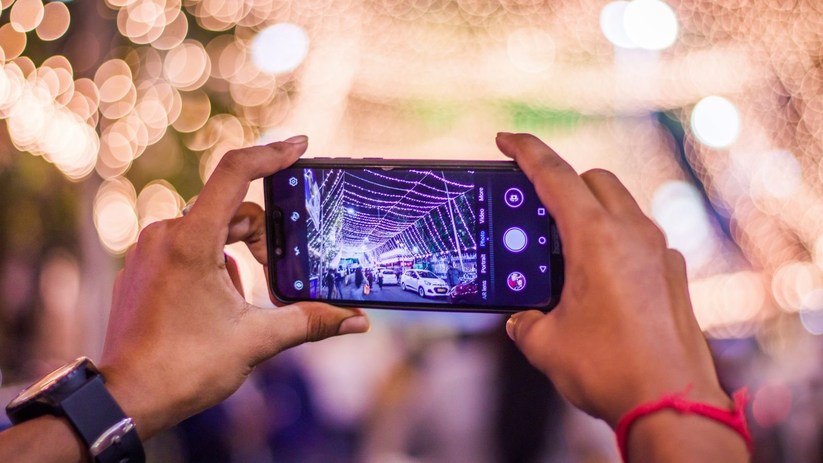 diwali photos on phone: hands taking a photo of festive lights with a smartphone