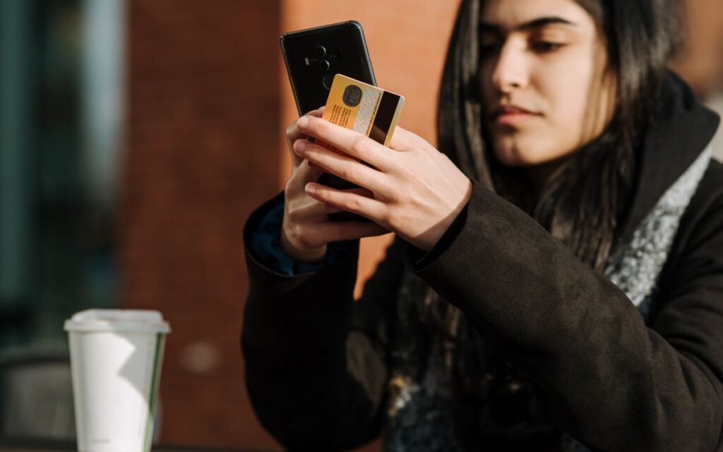 young woman checking a card while paying on her phone at a cafe table
