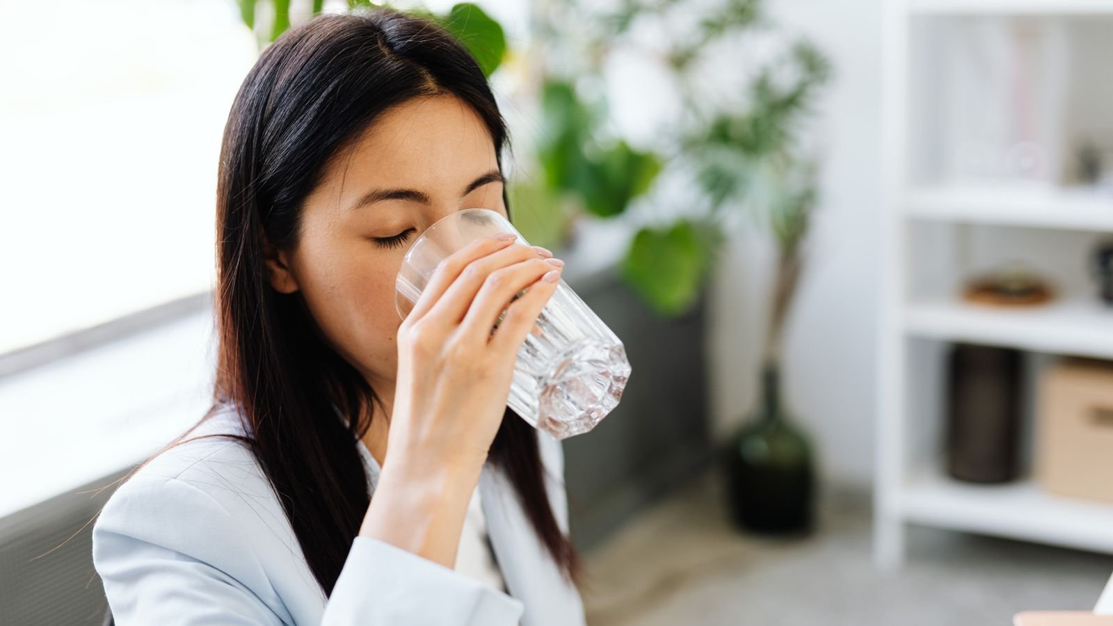 young woman drinking a full glass of water in a bright room