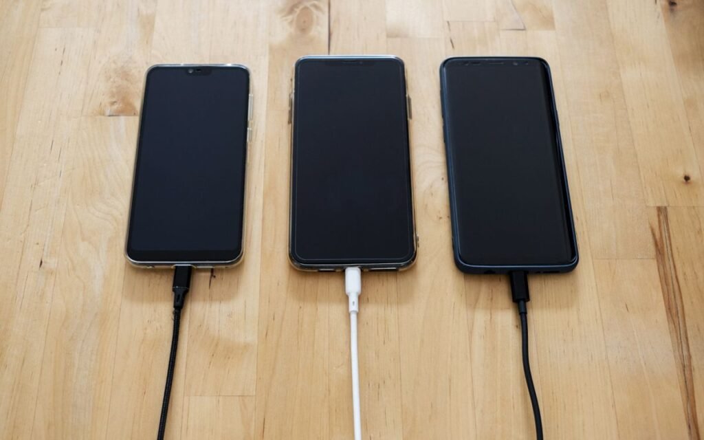Three phones charging side by side on a wooden table