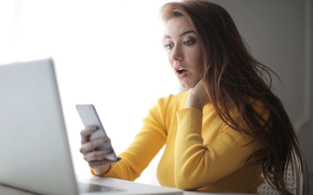 Woman checking her phone while working on a laptop
