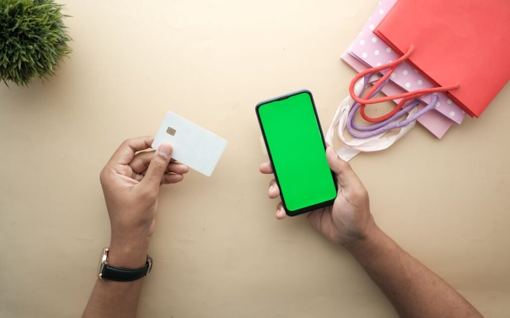 Hands holding a bank card and a smartphone next to festive shopping bags