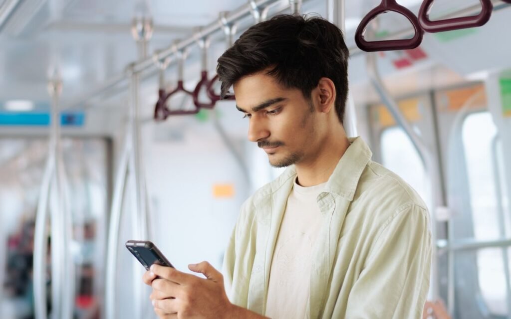 young man scrolling on his smartphone while standing in a metro train