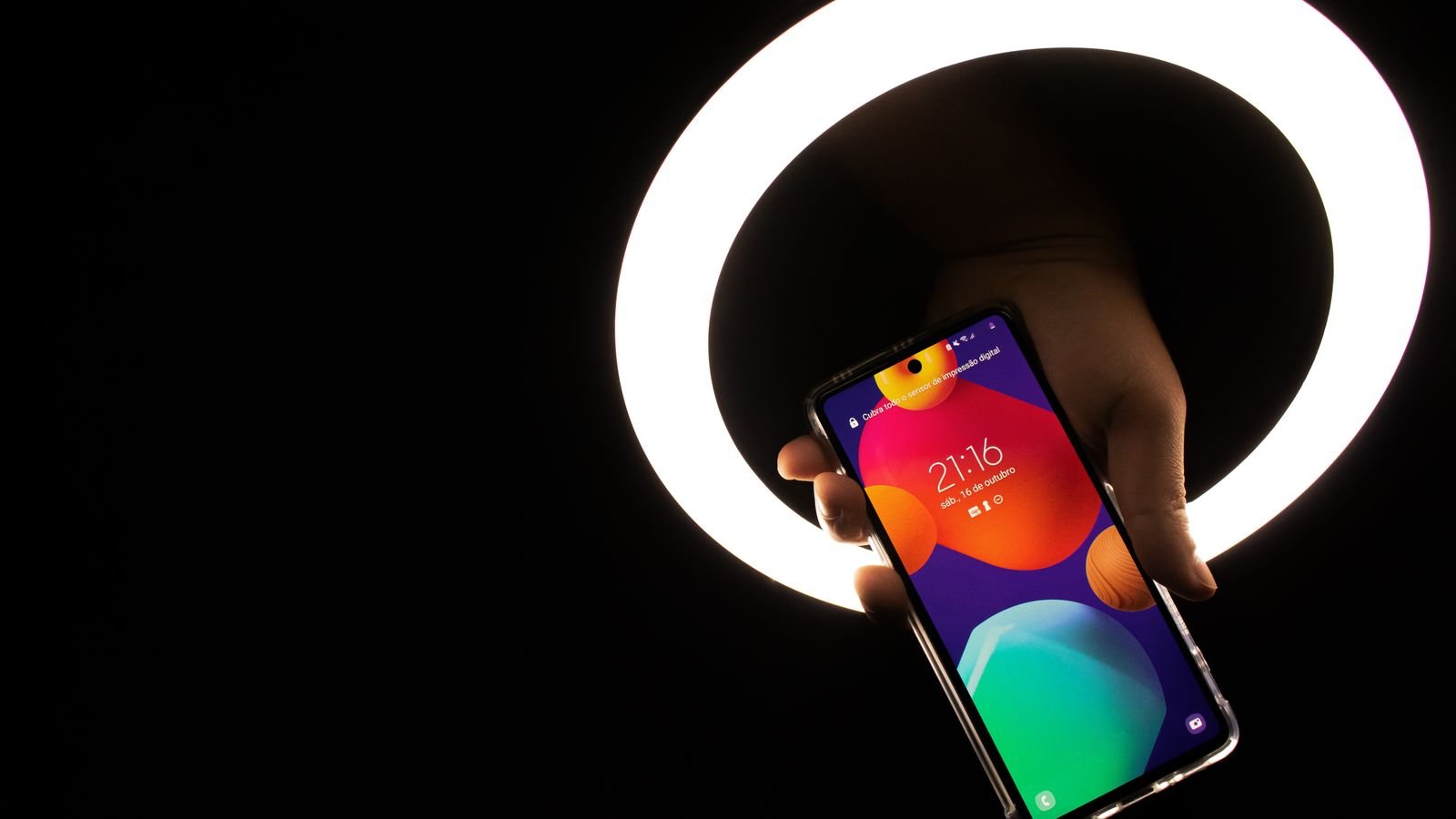 hand holding a Samsung Android phone with a colourful lock screen in front of a ring light