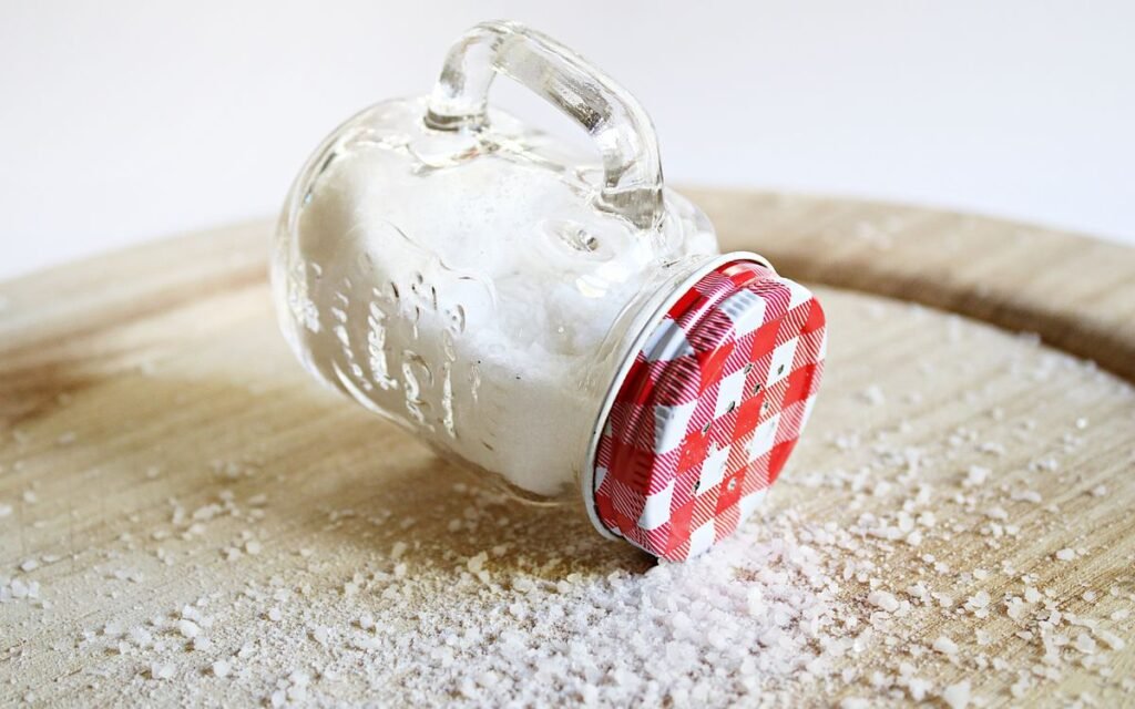 Glass jar of salt tipped over on a wooden board