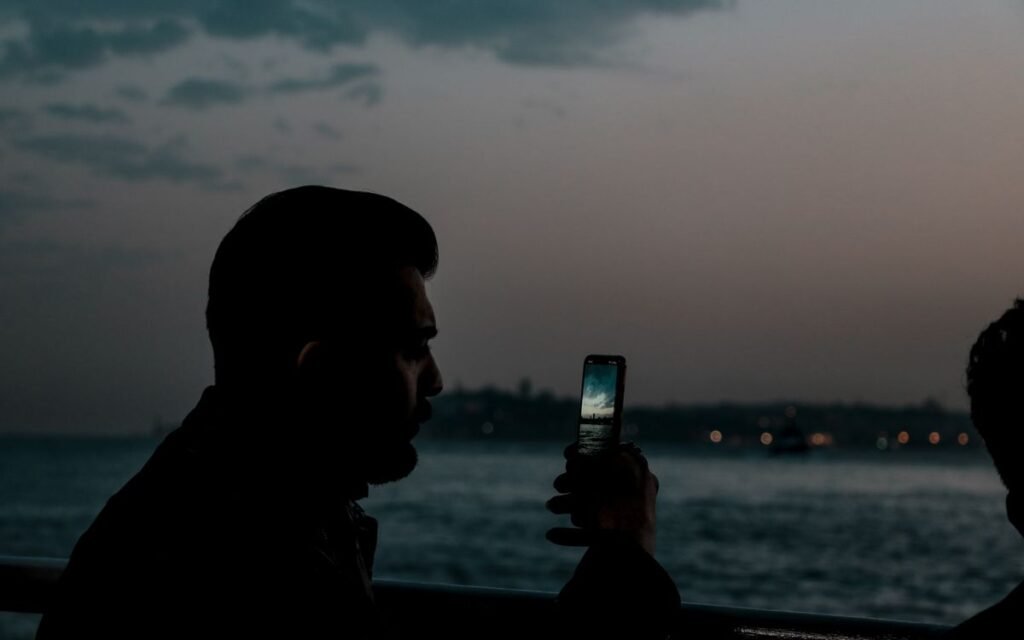 Man taking a phone photo of the sky over water at dusk