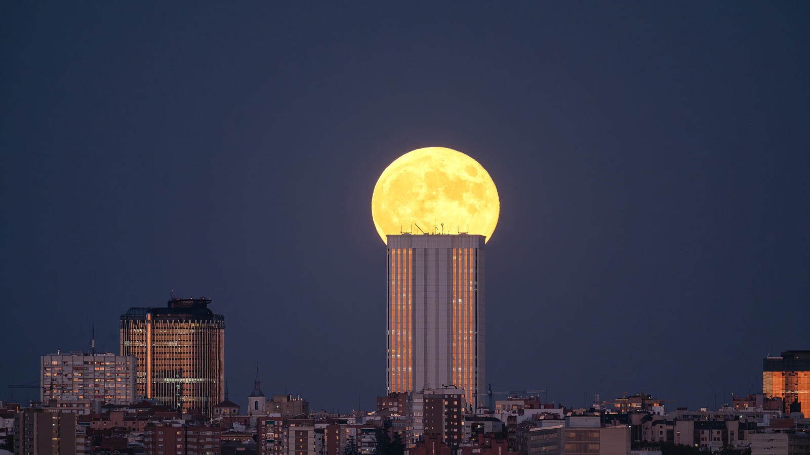 Hunter's moon: big yellow full moon rising behind a tower block at dusk