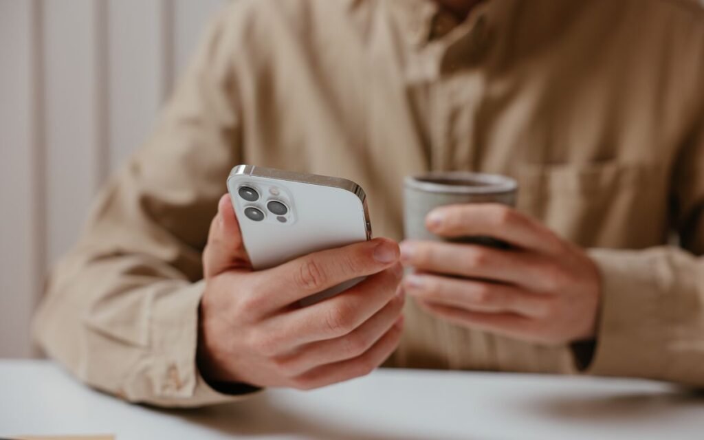 Person holding a silver iPhone beside a coffee cup