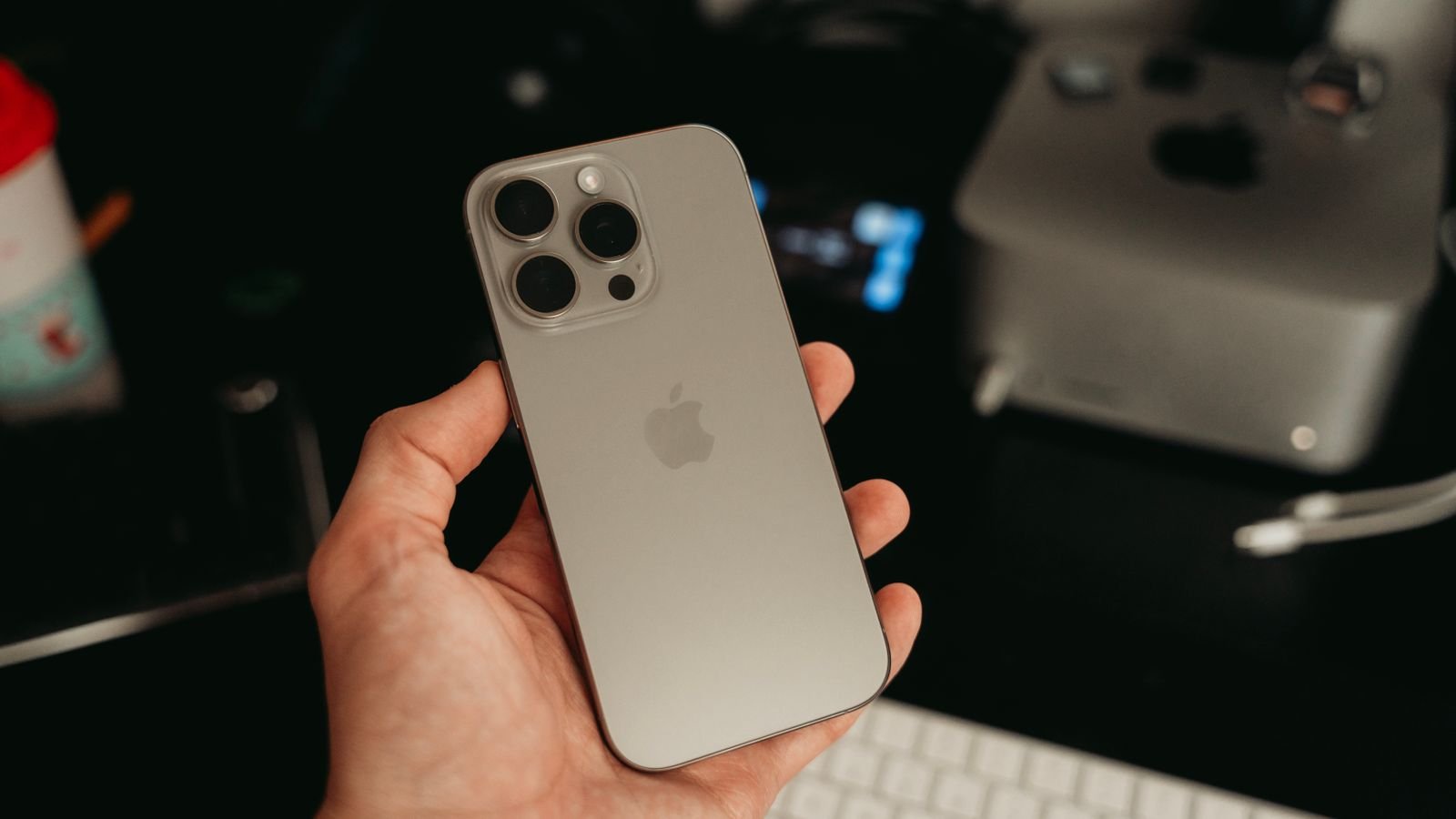 hand holding a titanium iPhone with its triple camera and Apple logo facing the camera