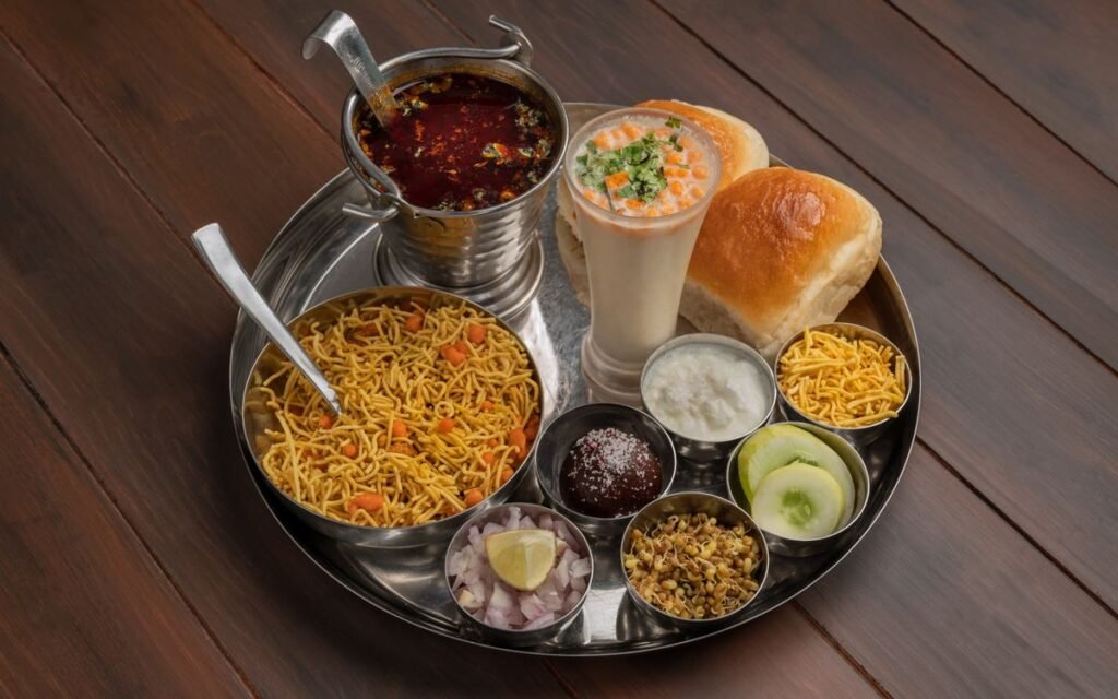 A steel thali with several small dishes, a lemon wedge and pav