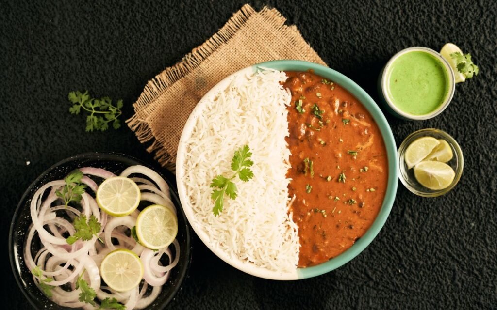 A plate of rice and bean curry with lemon slices and onion rings on the side
