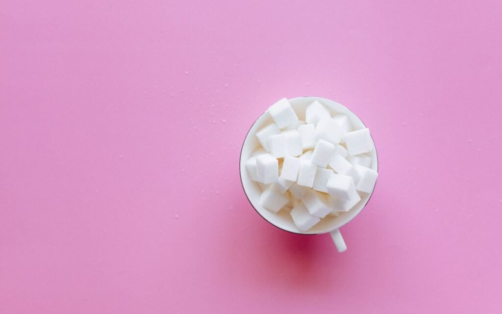 White sugar cubes in a small cup on a bright pink background
