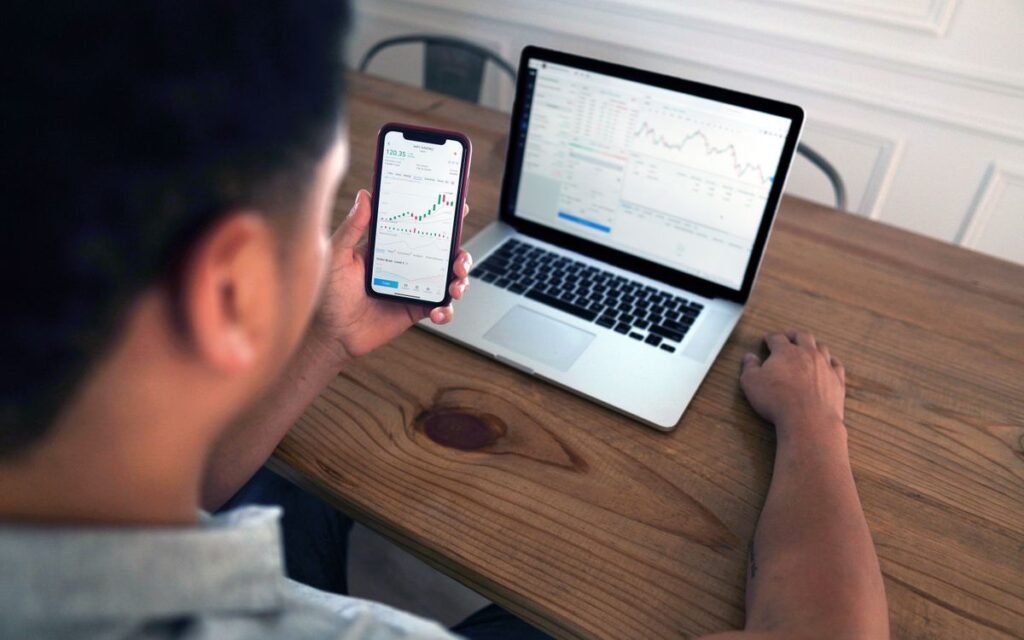 Man reviewing stock charts on a phone at a wooden table