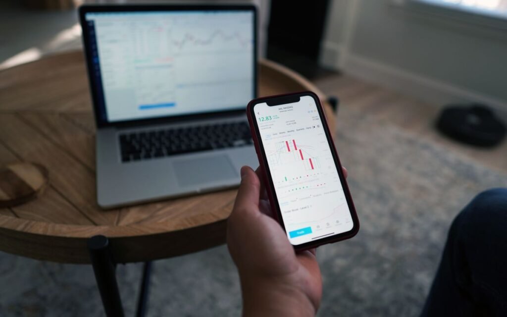 Person checking stock charts on a phone with a laptop nearby