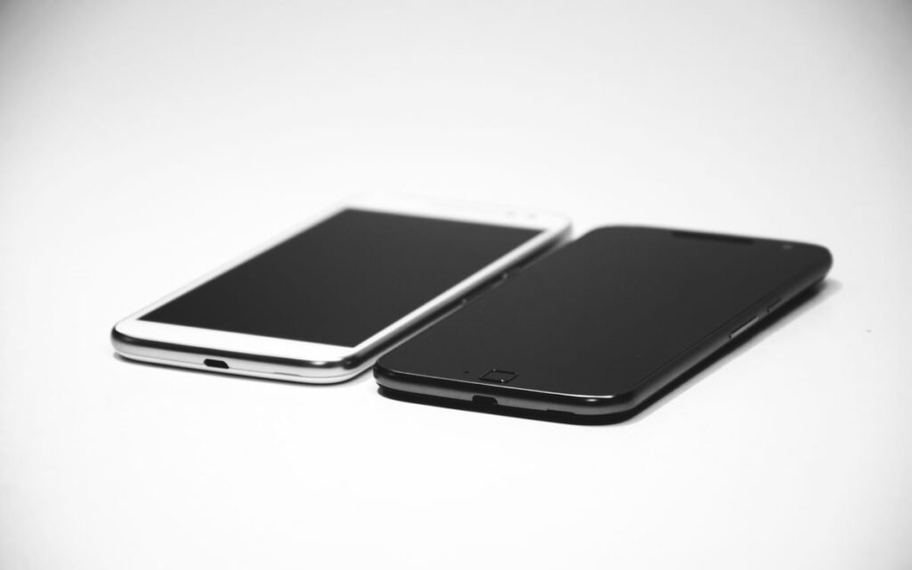 A black and a white smartphone side by side on a white surface
