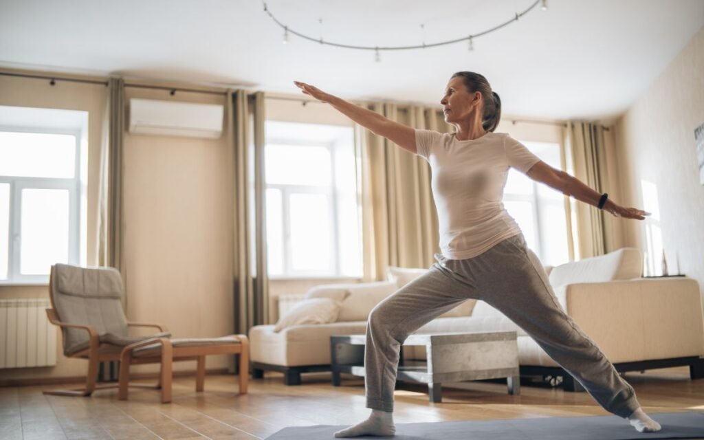 older woman doing a standing yoga stretch on a mat in her living room