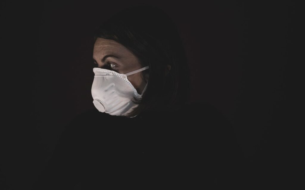 Woman wearing a white N95 respirator against a dark background