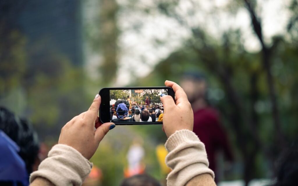 hands holding a smartphone to film a crowd at an outdoor event