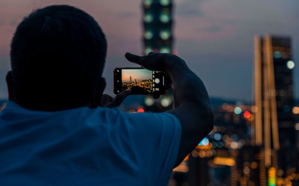 Man holding up a smartphone to photograph a city skyline at dusk