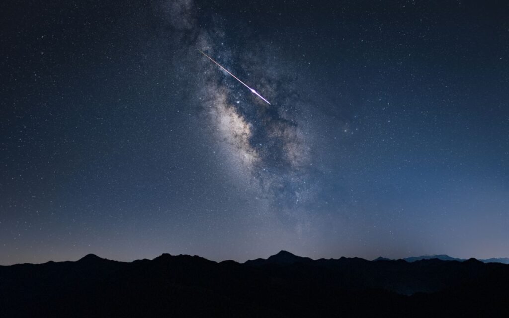 A shooting star crossing the Milky Way above a mountain ridge