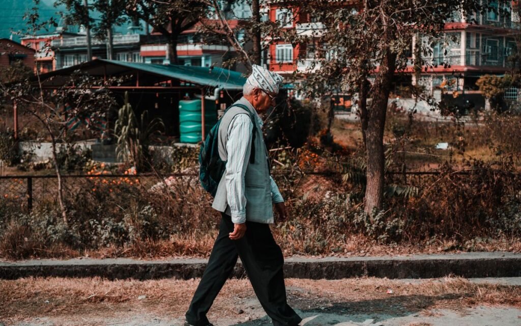 Older man in a cap walking along a tree-lined street