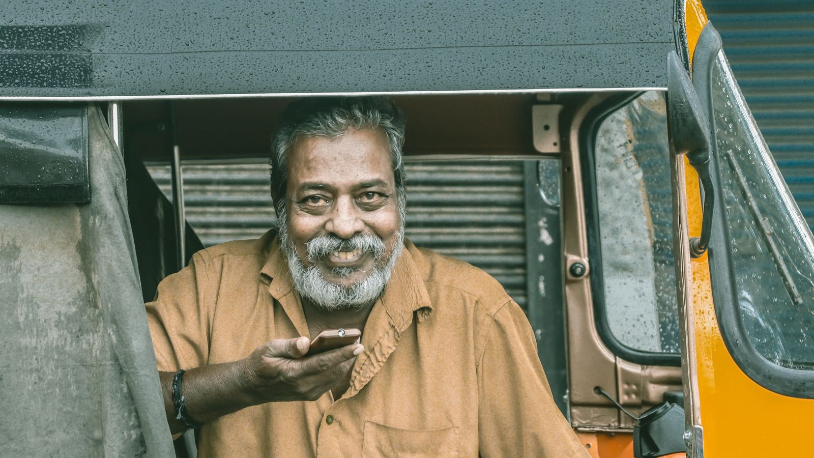 phone safety for parents: smiling older Indian man holding a smartphone in an auto-rickshaw