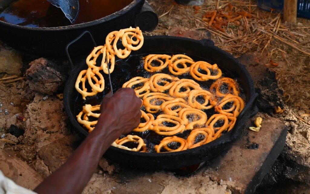 Jalebi frying in a large pan of oil over a wood fire