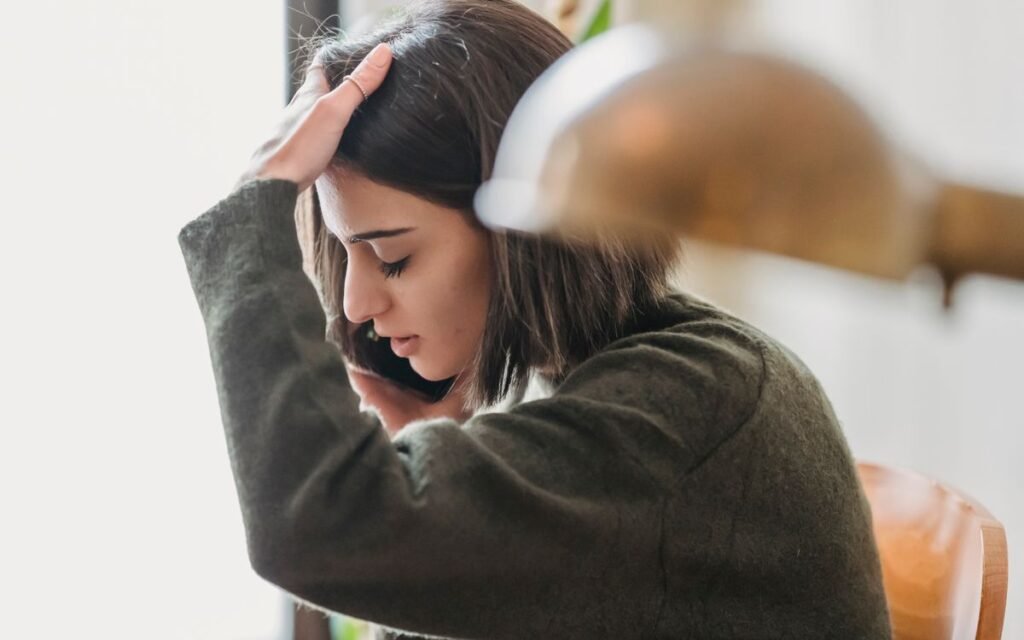 Woman holding her head while talking on a phone at home