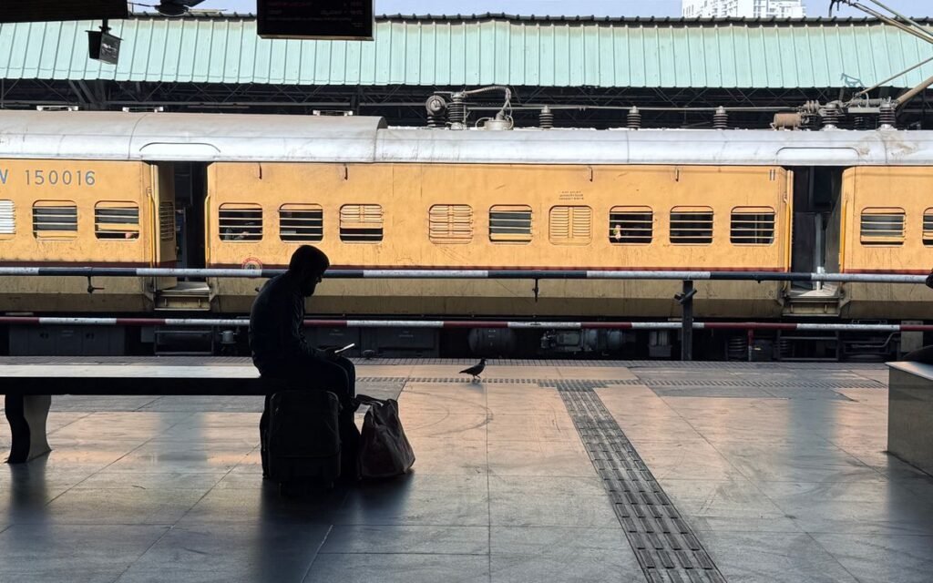 A traveller sitting with luggage on a quiet Indian railway platform