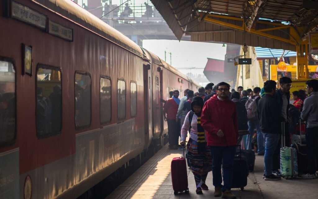 Passengers with luggage on a crowded Indian railway platform beside a train