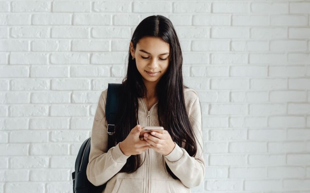 Young woman with long hair texting on a smartphone against a white brick wall