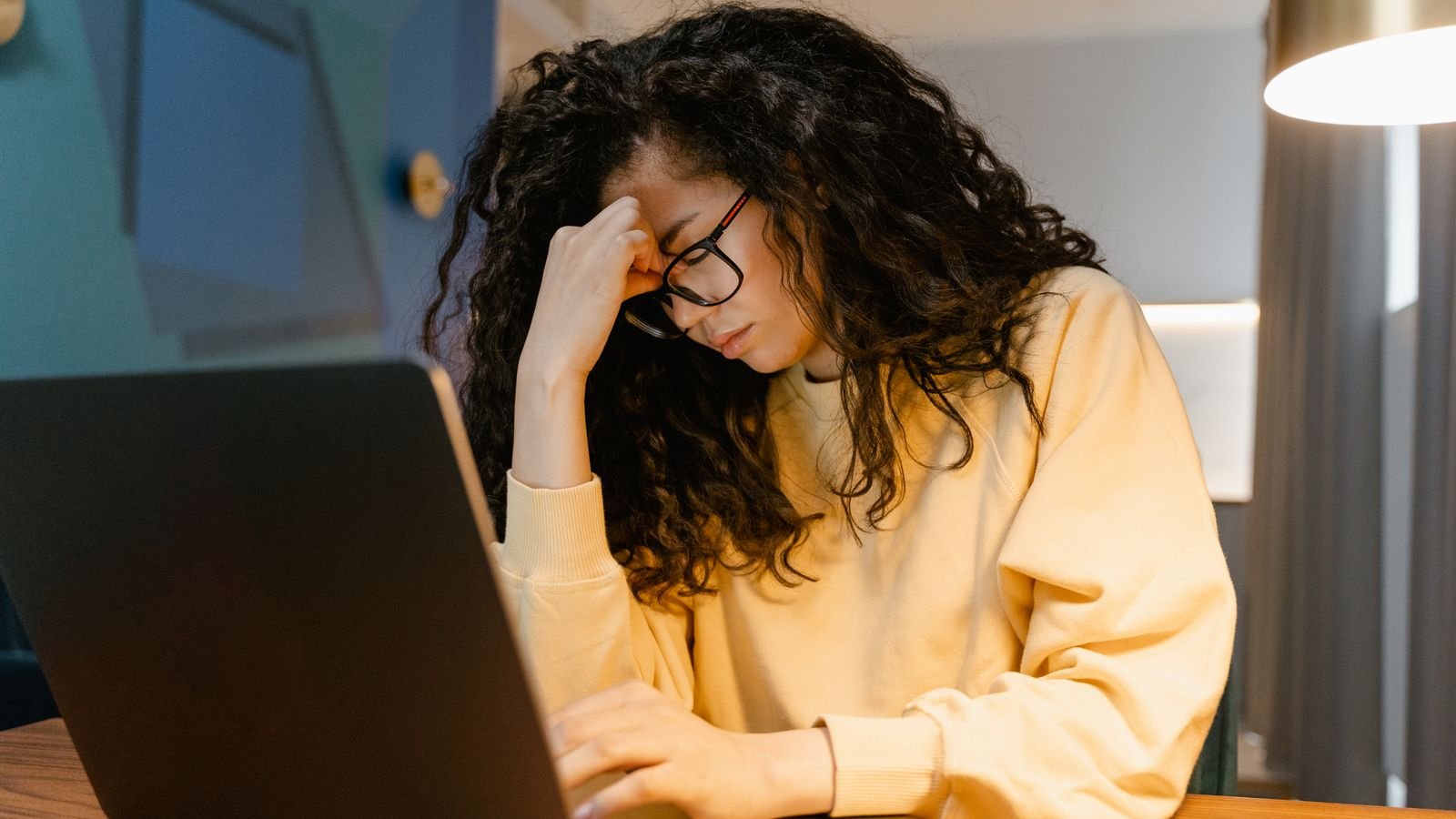 woman at a laptop holding her head, looking exhausted, a common sign of vitamin B12 deficiency